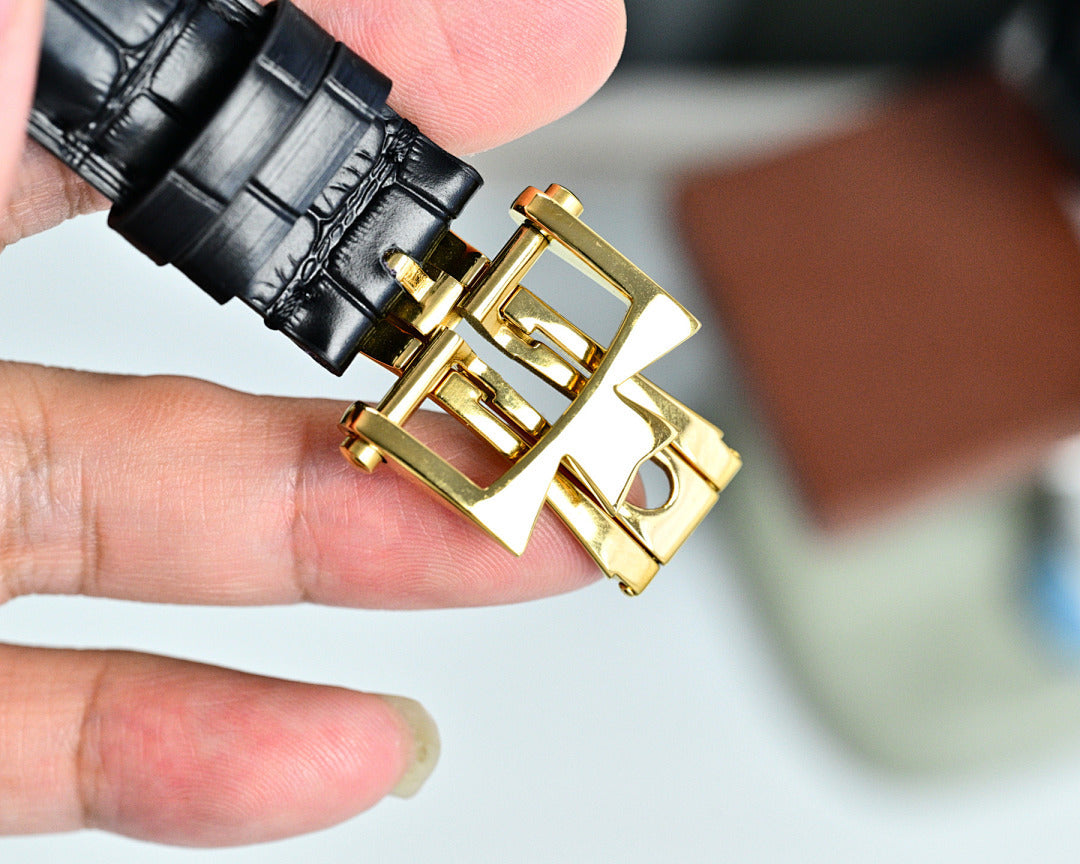 Black leather watch strap with gold-tone deployant clasp, wristwatch close-up