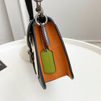 Coah bag side view with black exterior and tan lining, green tag keychain
