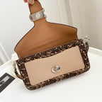 Coah bag with brown handle strap, beige front, and oval turn-lock on patterned flap trim.