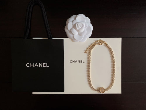 Gold-tone chain necklace with oval drape, round logo medallion, and small bow detail