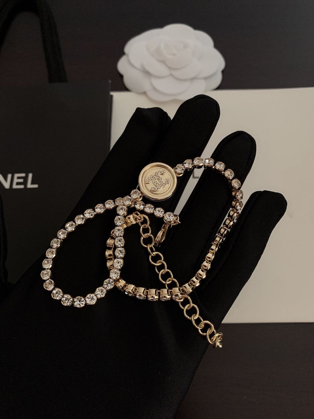 Gold-tone rhinestone bracelet with round logo medallion and layered linked chain charms