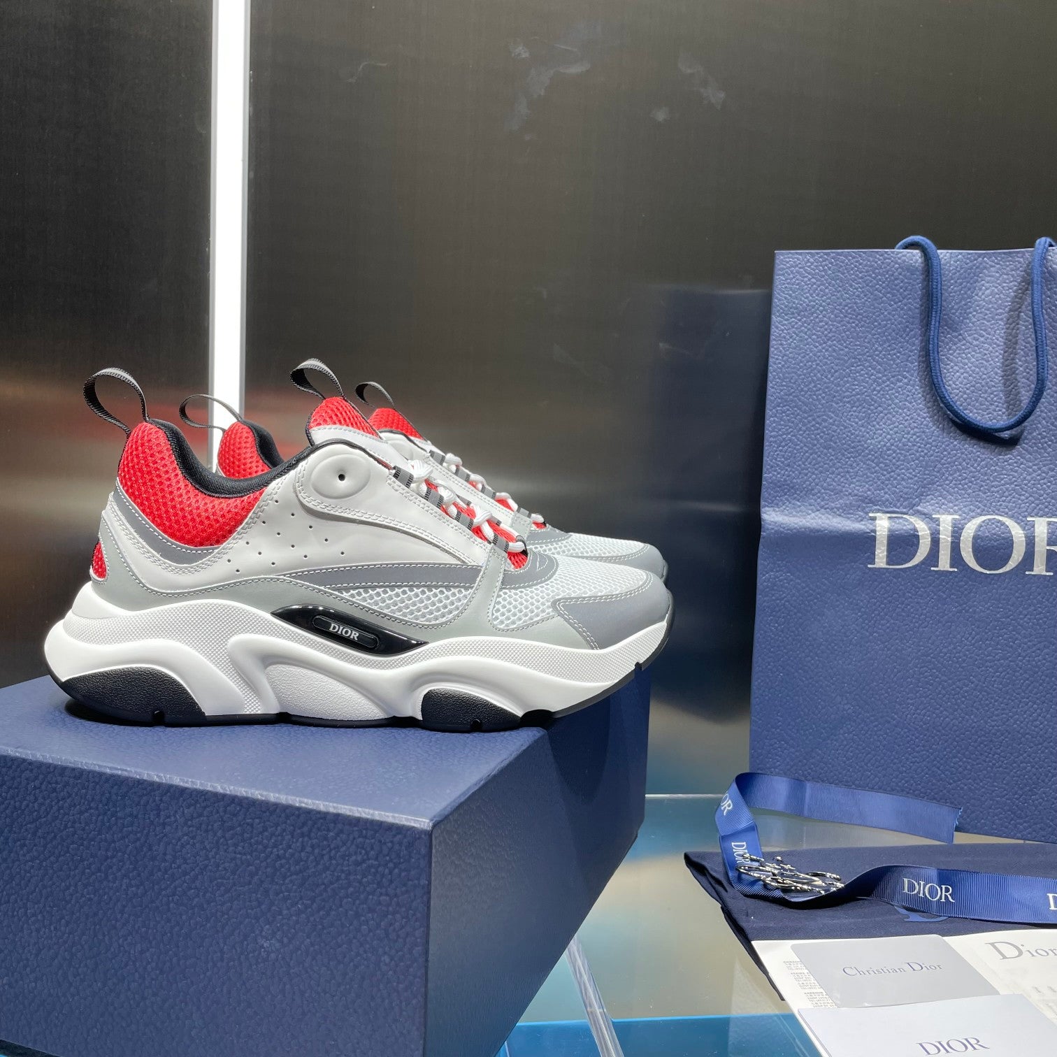 White sneakers with red tongue, blue laces, and black side trim on a box.