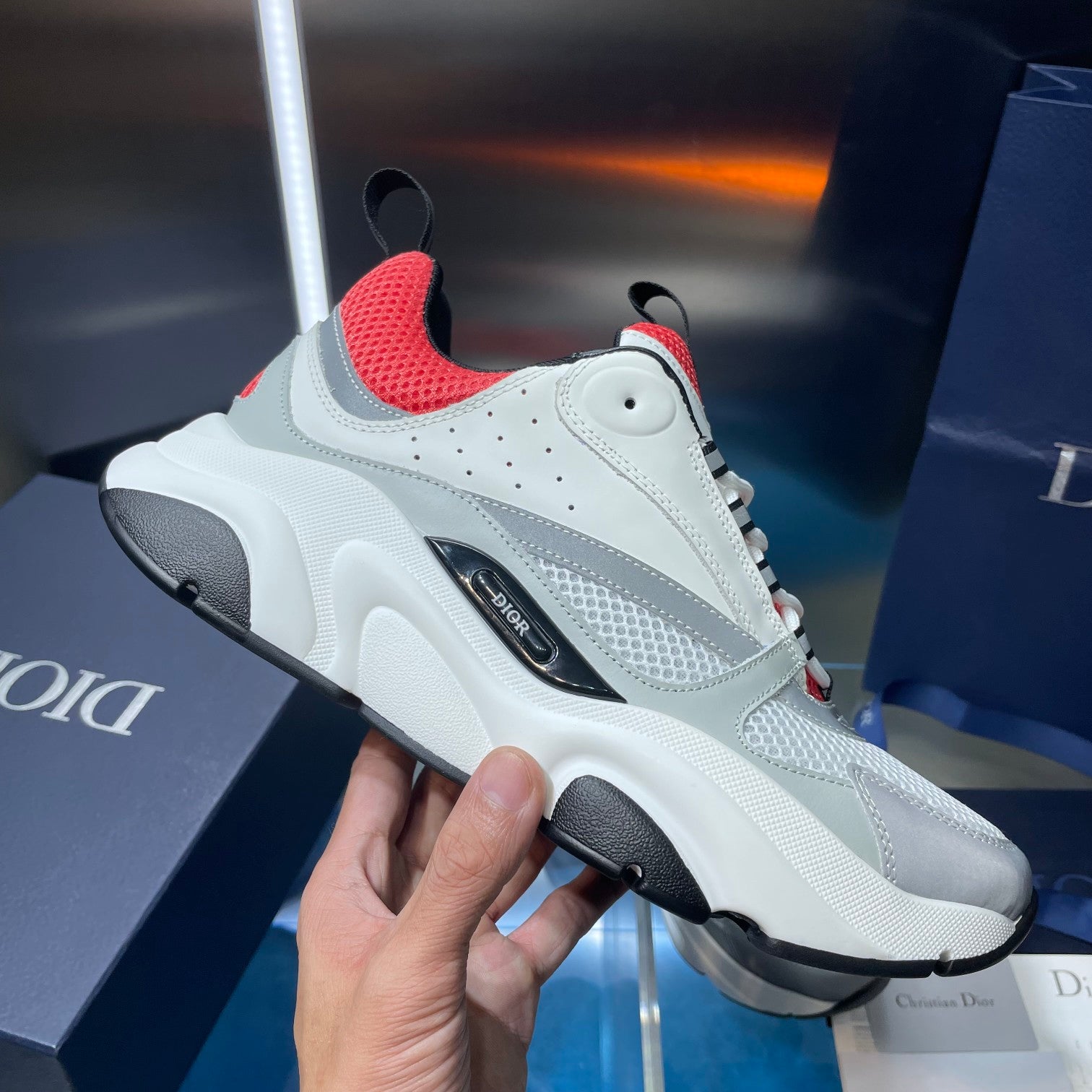 White sneaker with red collar lining, textured panels, and black logo stripe.