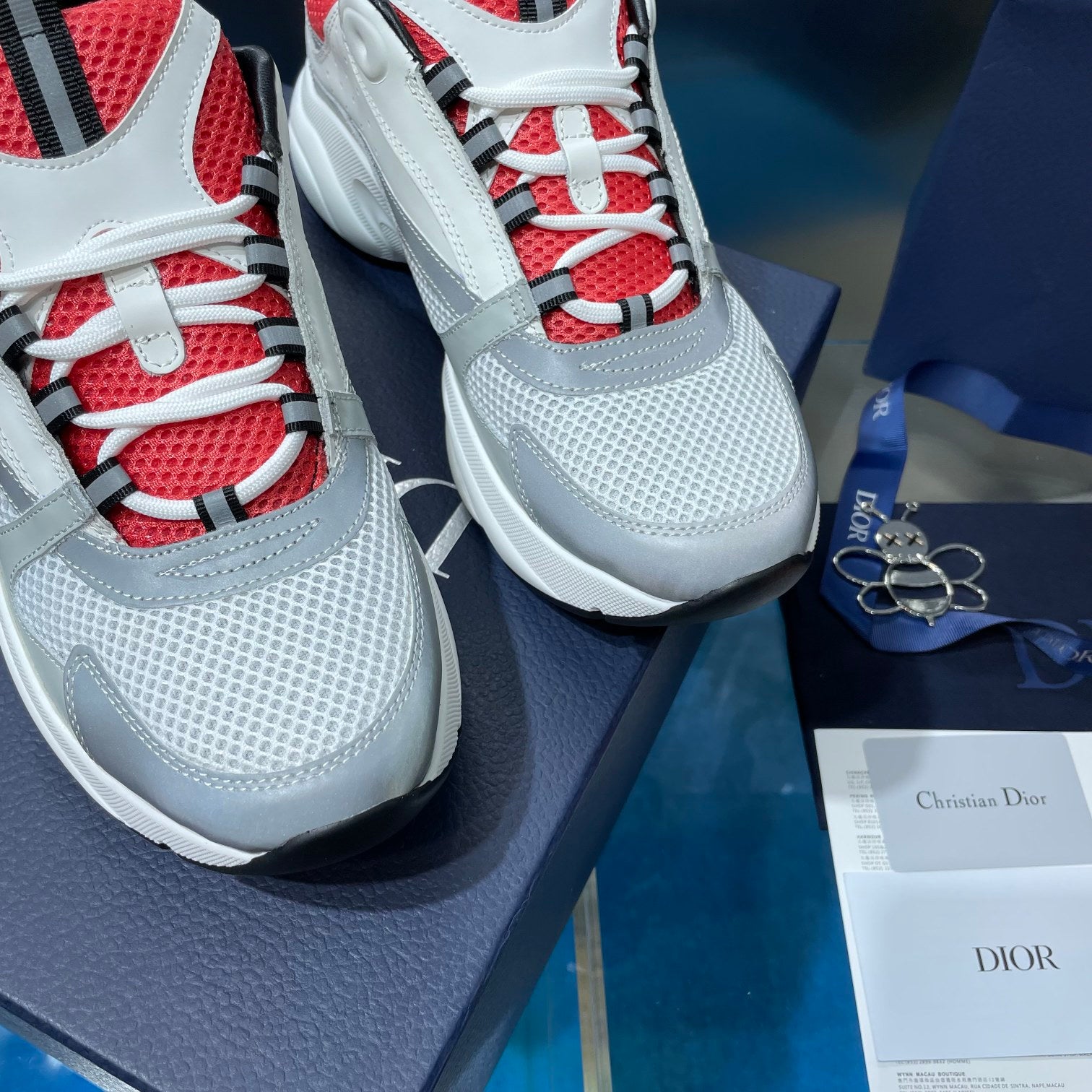 Close-up of white sneakers with red-and-black eyelets and blue-and-white laces.