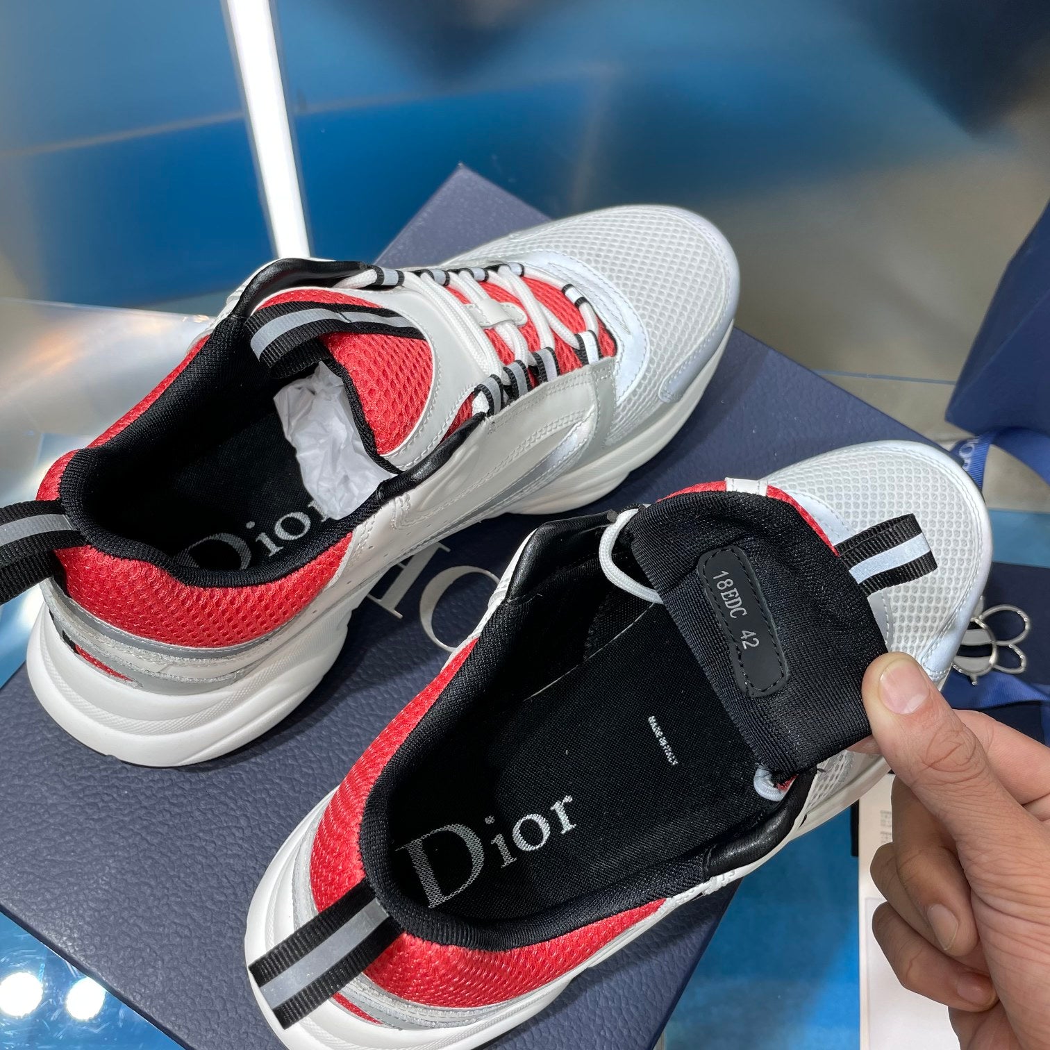 White sneakers with red lining and black interior collar, hand holding one shoe.