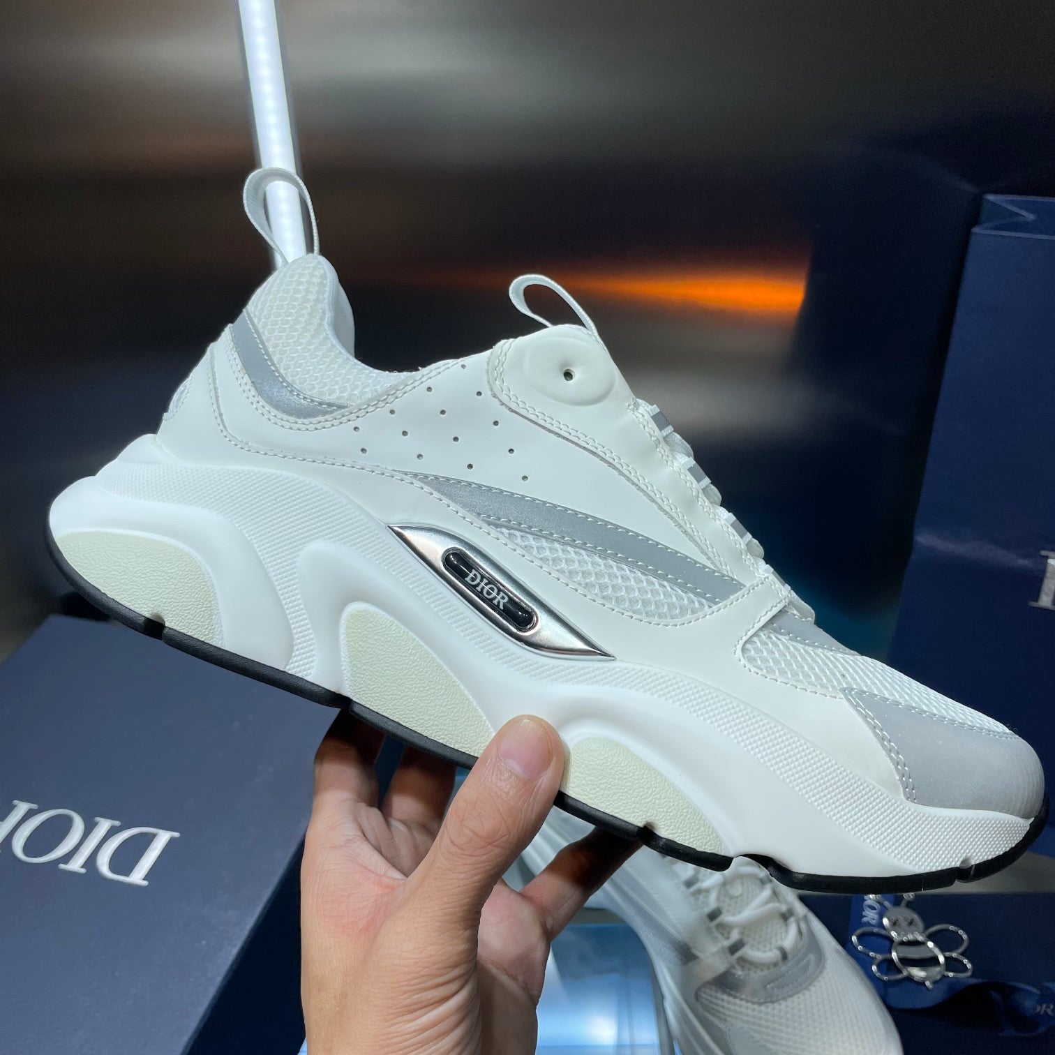 White lace-up sneaker held in hand, cushioned sole and logo badge