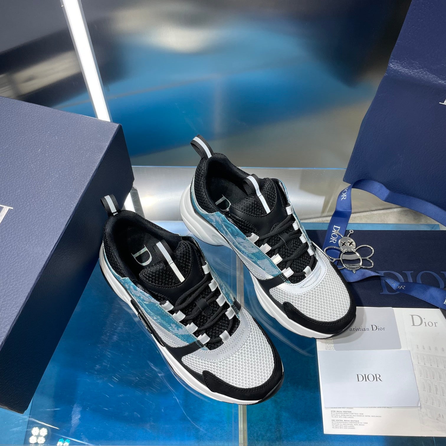 Dior unisex sneakers on box, featuring black-and-white uppers with light blue accents