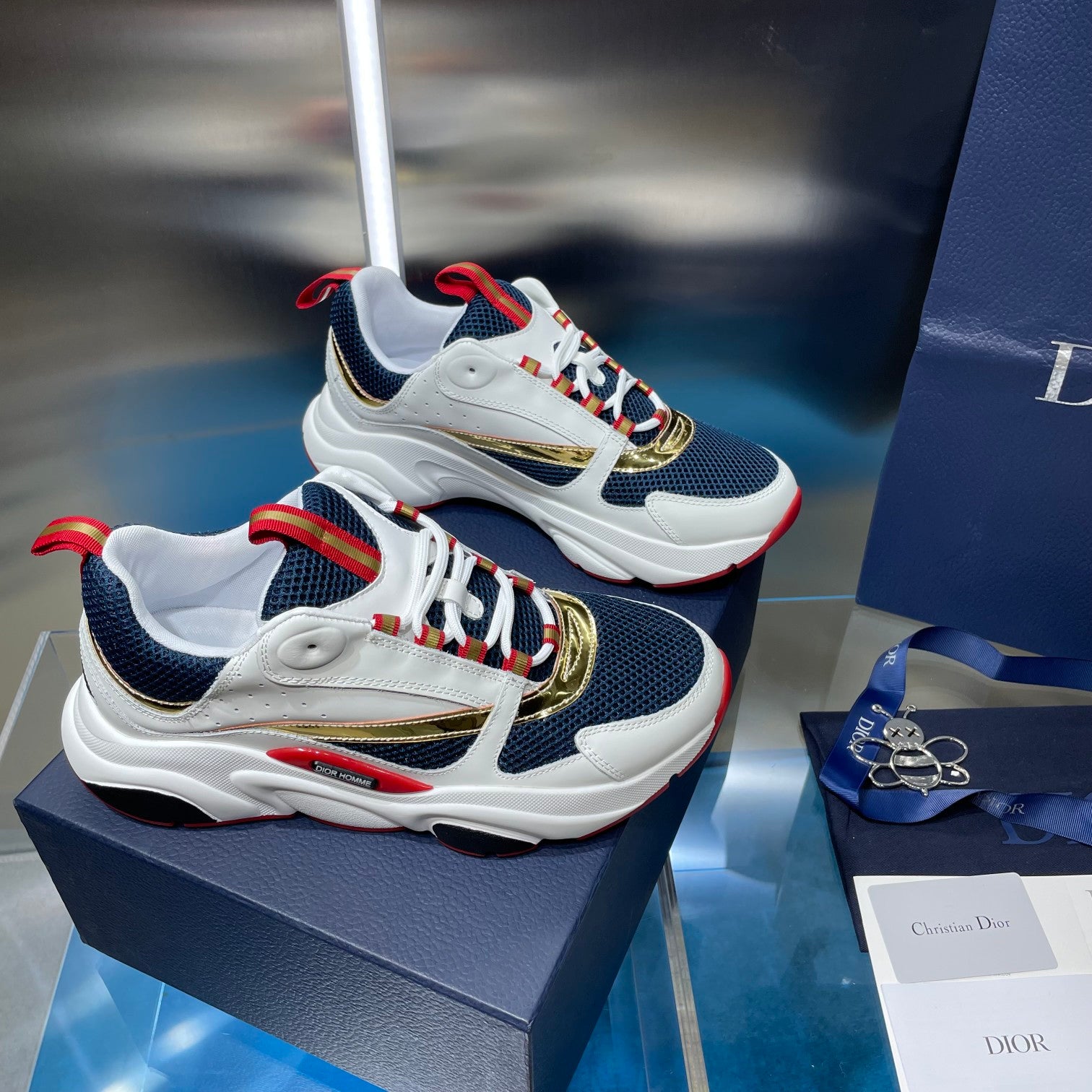 Dior unisex sneakers on box, navy and white with gold accent and red laces