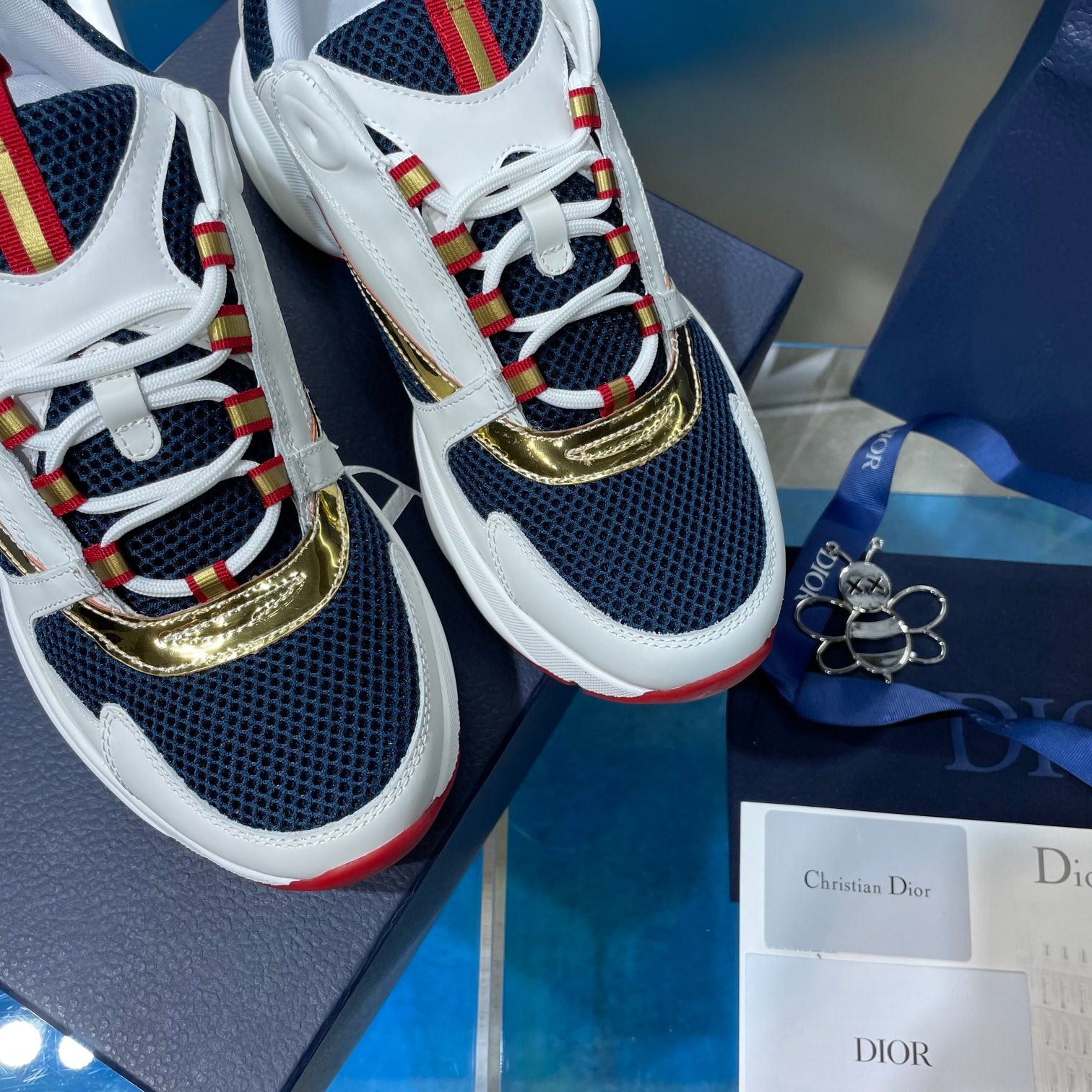 Dior unisex sneaker close-up, navy mesh with gold trim and red ribbon laces