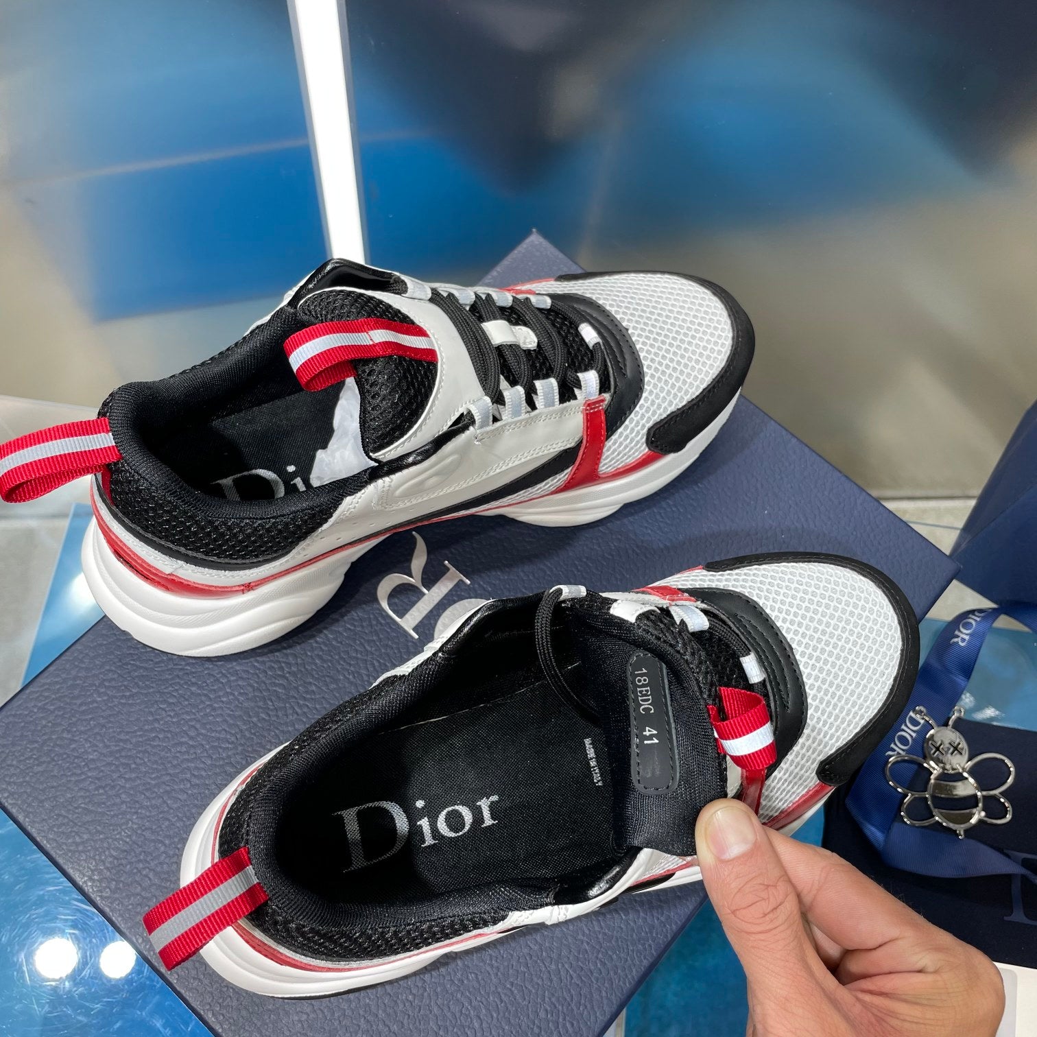 White and black sneakers with red stripe trim and padded collar; hand holding heel.