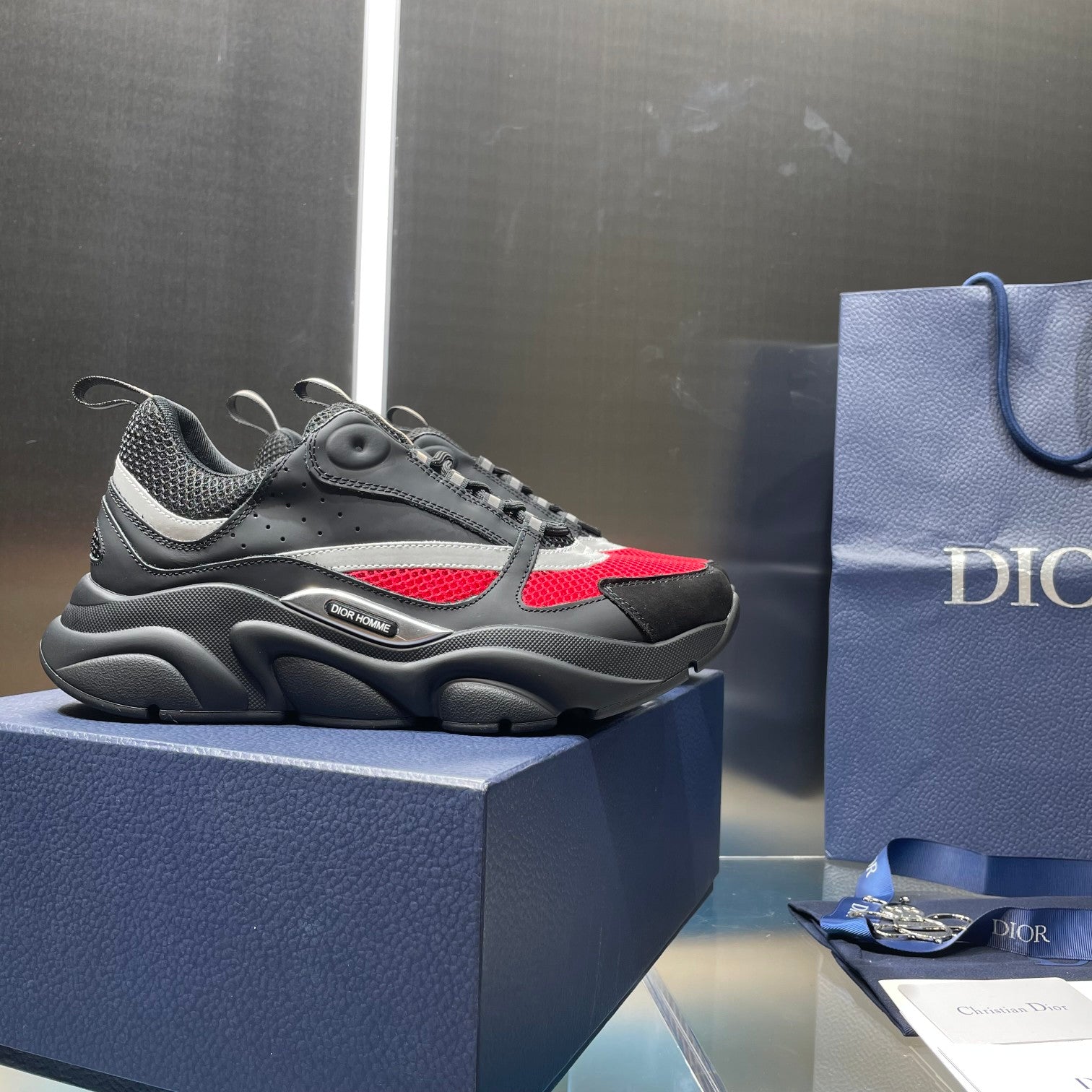 Unisex Dior lace-up sneakers on box, dark gray mesh with red and white side stripe
