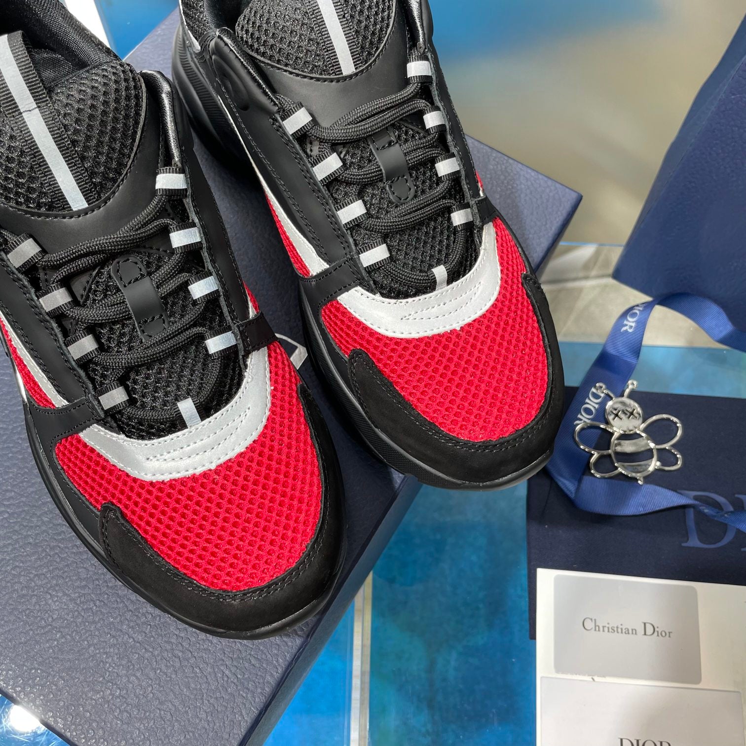 Unisex Dior lace-up sneakers close-up, black mesh with red toe panel and white mid stripe