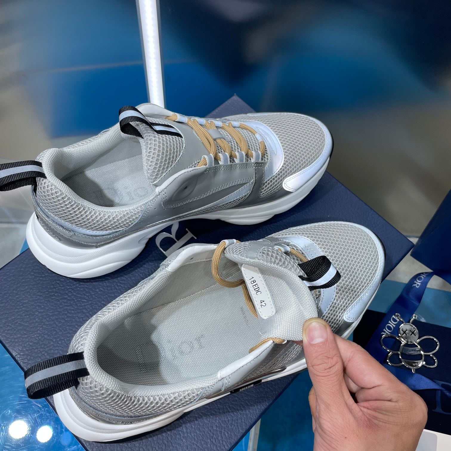 Unisex sneakers with light gray mesh and gold laces; hand holding shoe