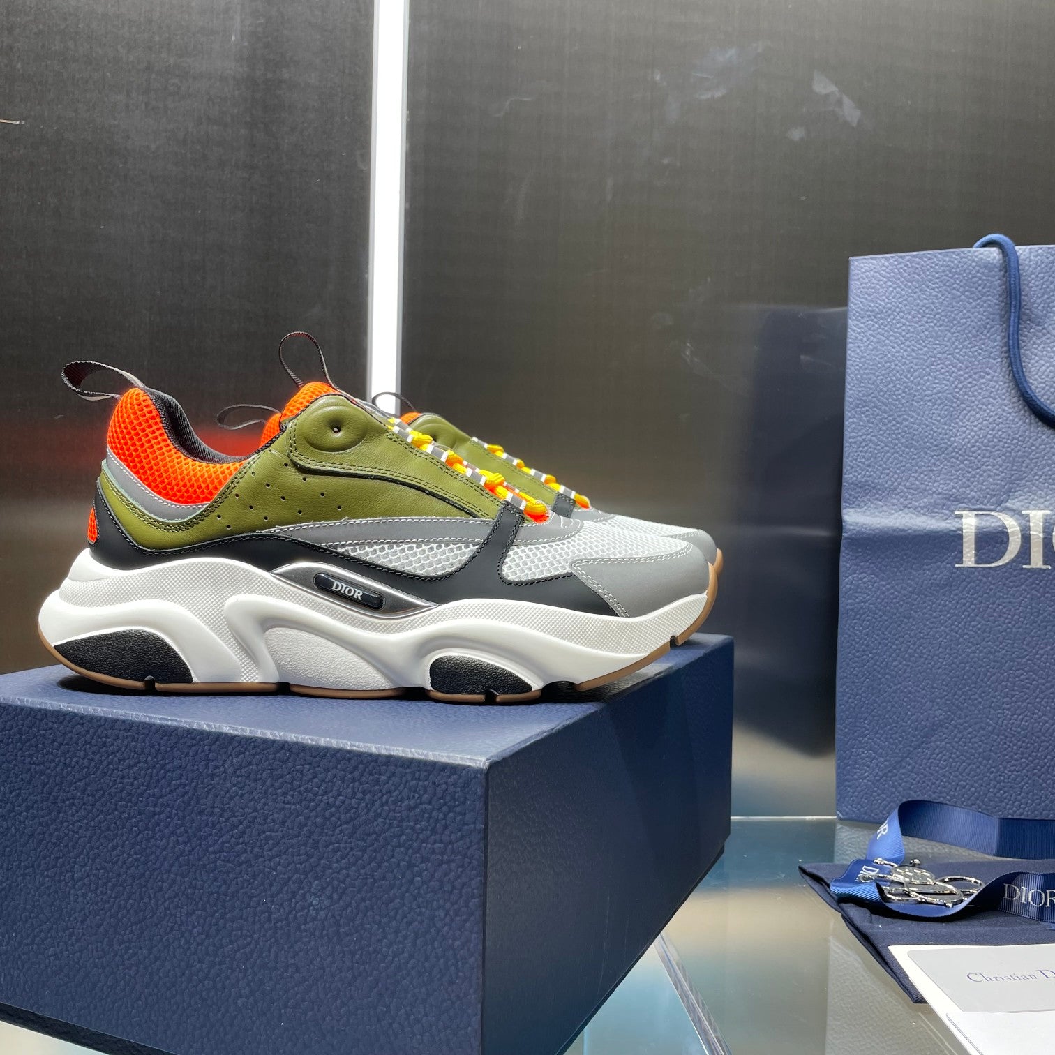 Dior unisex sneakers on a box: white sole, olive panels, orange lining, rainbow laces