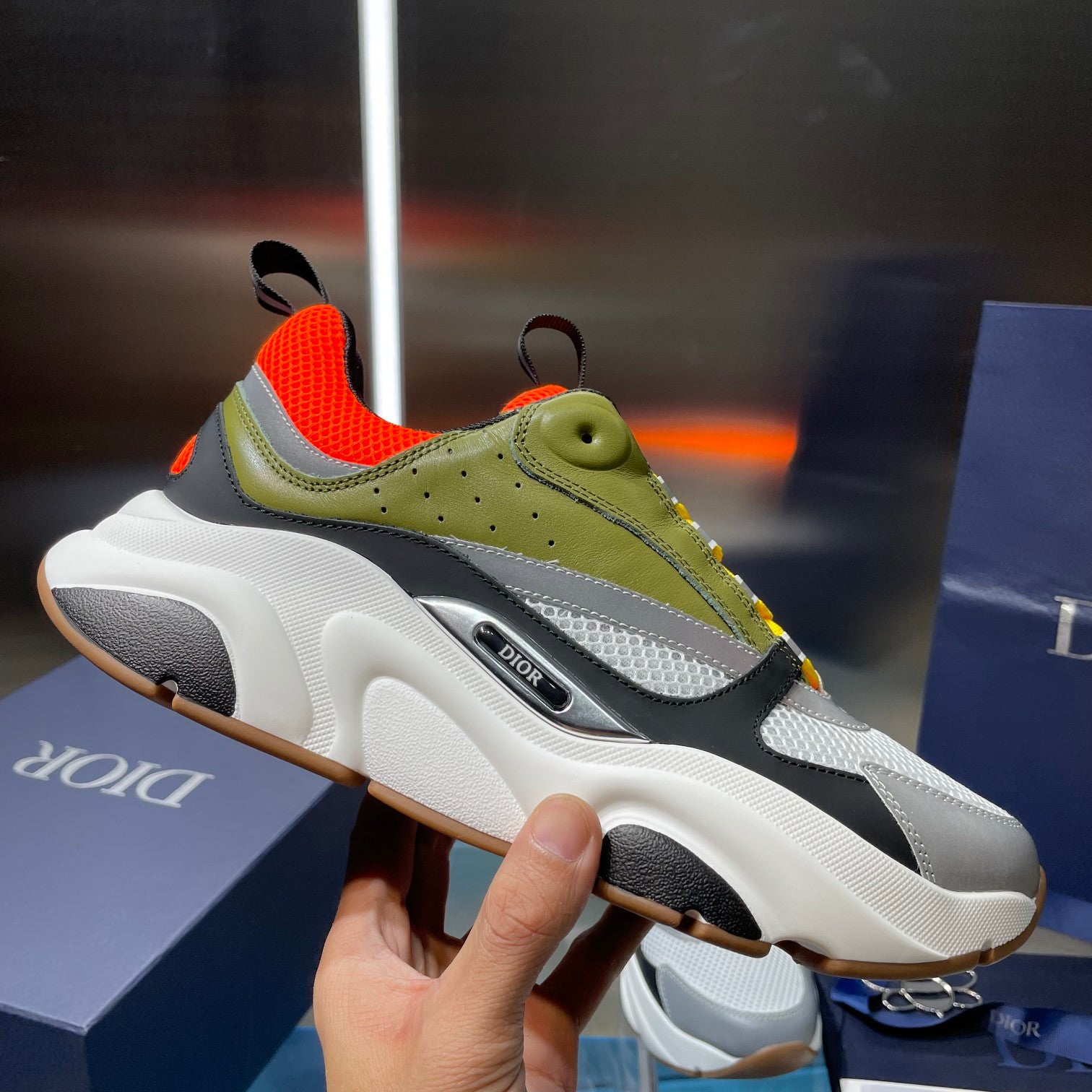 Dior unisex sneakers close-up: thick white sole, olive upper, orange heel, logo patch