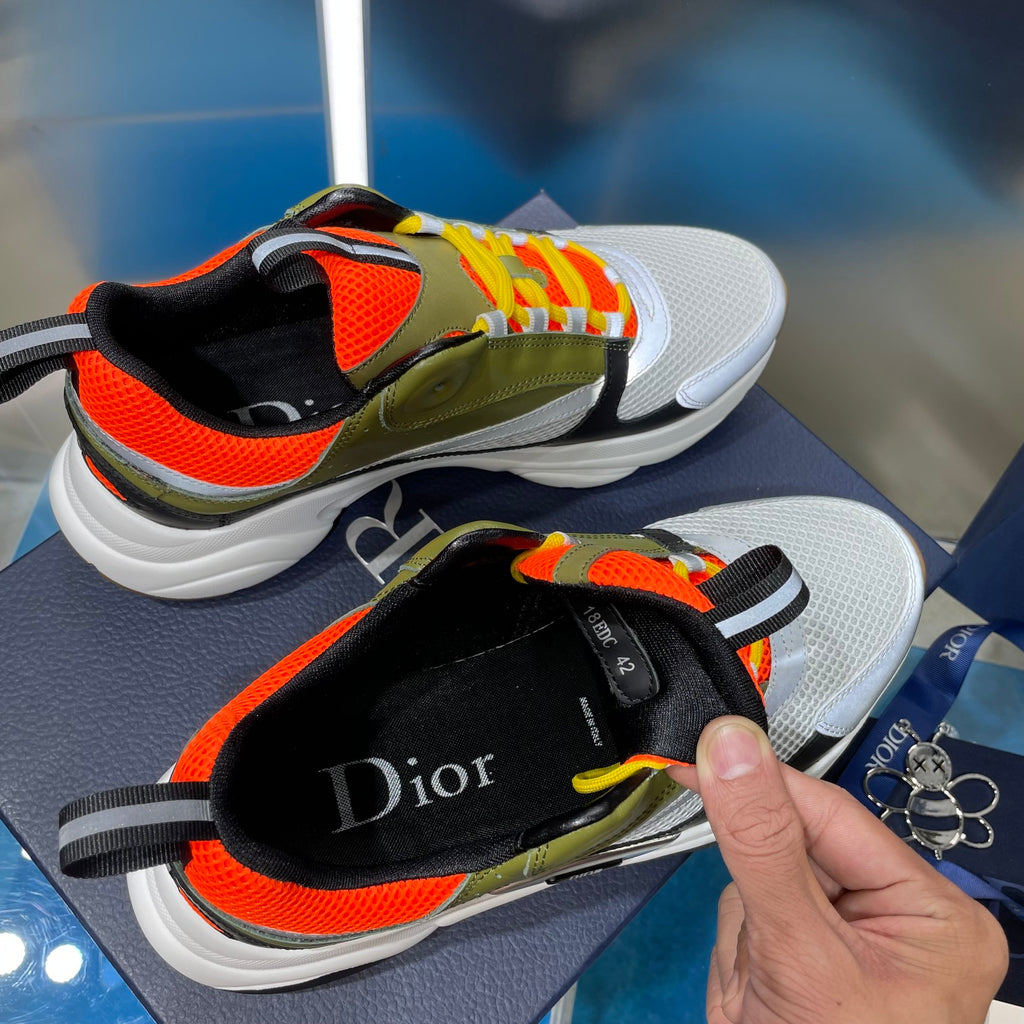 Dior unisex sneakers close-up with hand: olive and orange upper, white sole, lace detail