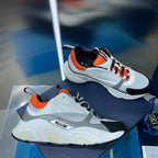 Dior unisex sneakers in white with orange accents and black toe panel, lace-up design.