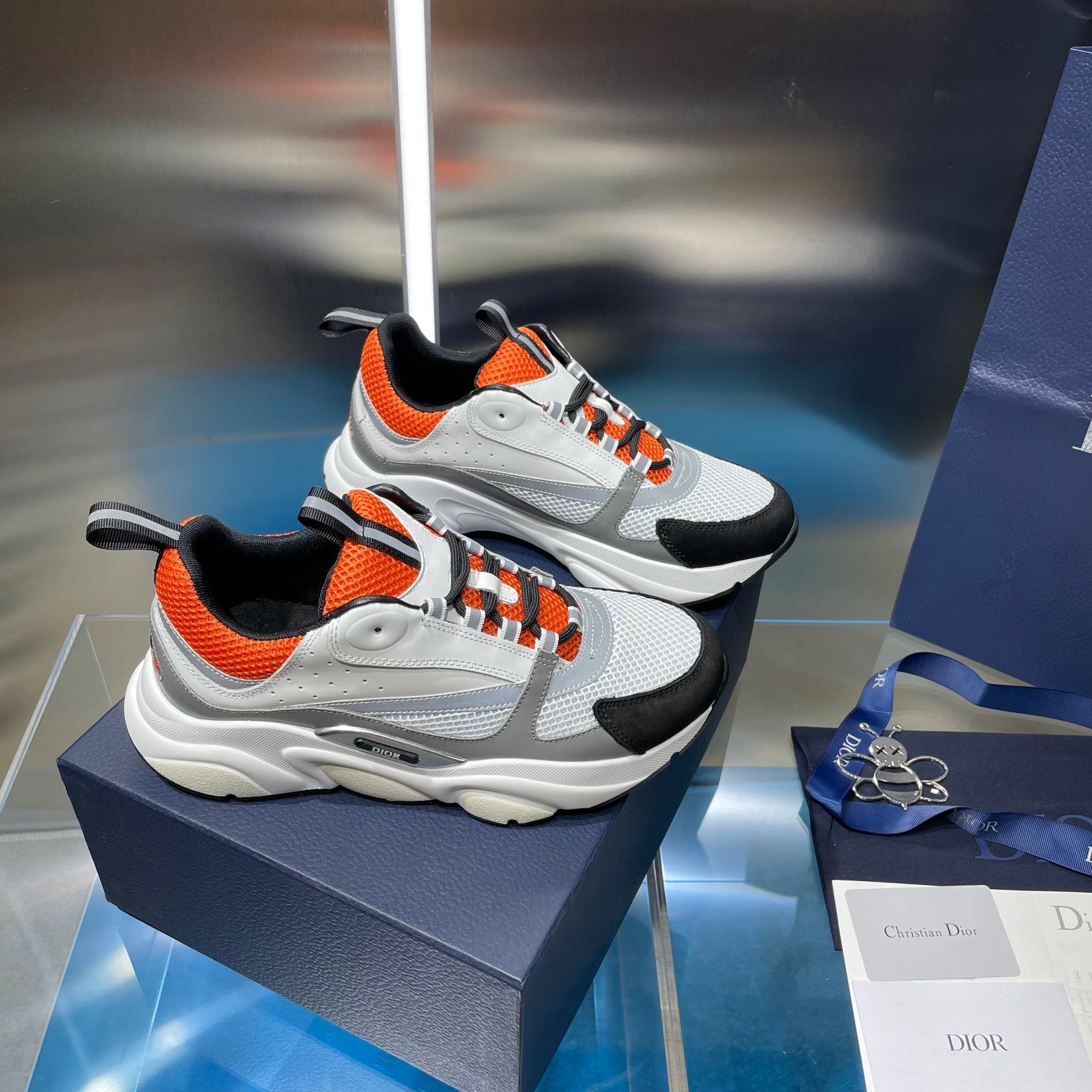 Dior unisex sneakers pair, white upper with orange collar and black overlays, lace-up.