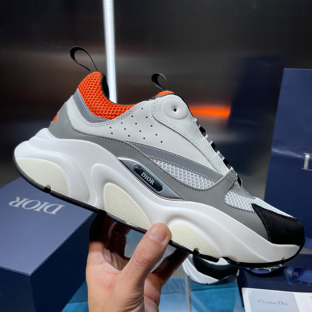 Dior unisex sneaker close-up, white upper with orange collar and gray-black logo trim.