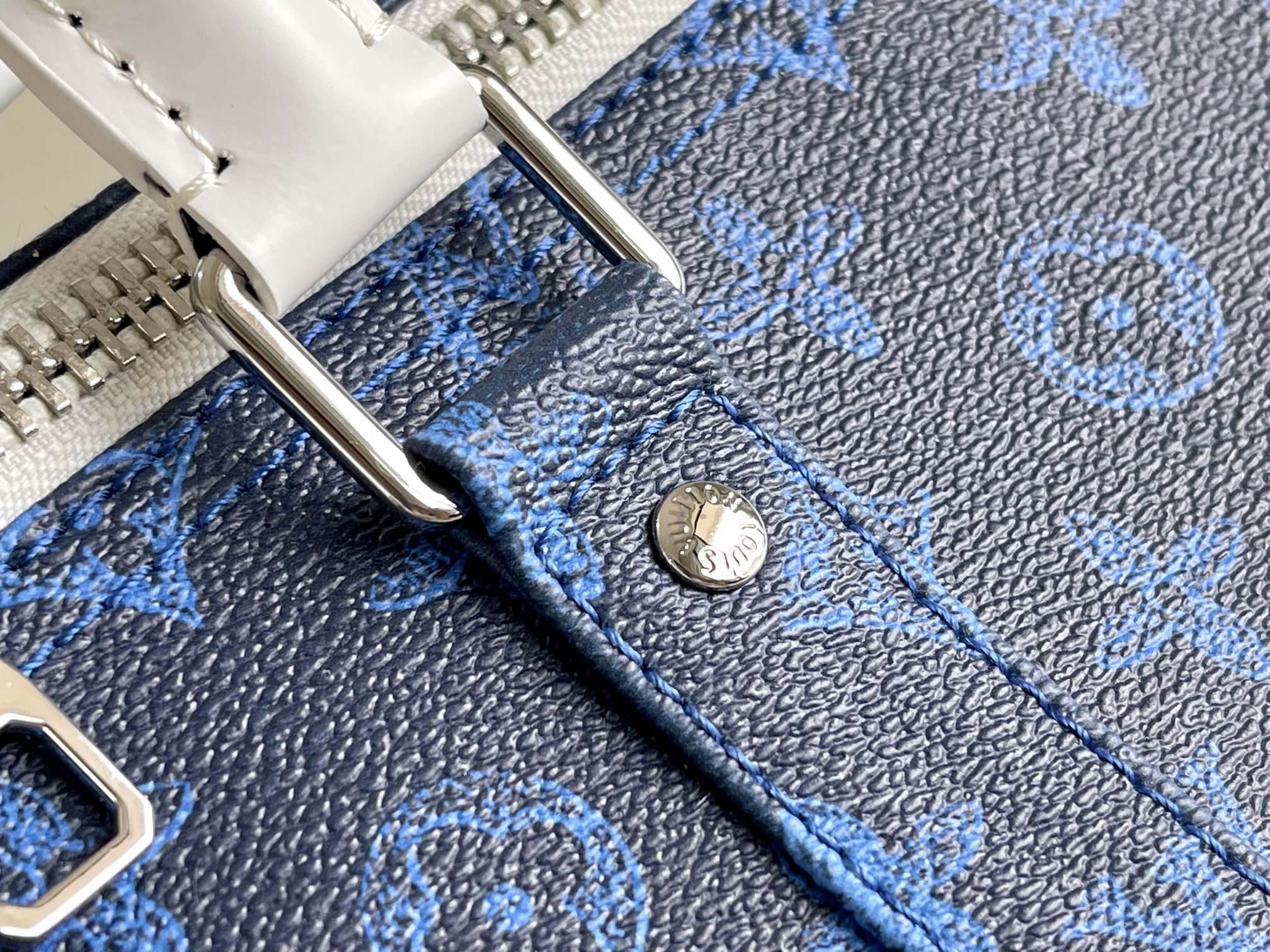 Blue monogram duffel bag close-up with white metal snap and stitched trim.