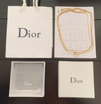 Gold chain necklace with charm in a white Dior gift box and pouch.
