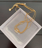 Gold chain necklace set with pearl charm, laid on a white jewelry box cushion.