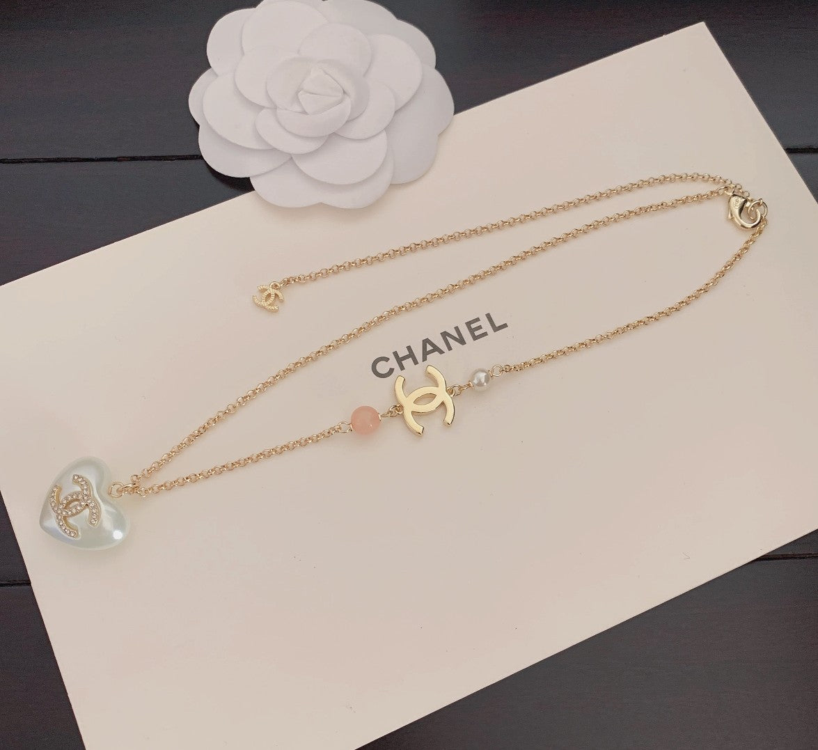Layered gold-tone necklaces with heart pendants, Chanel logo, pink bead