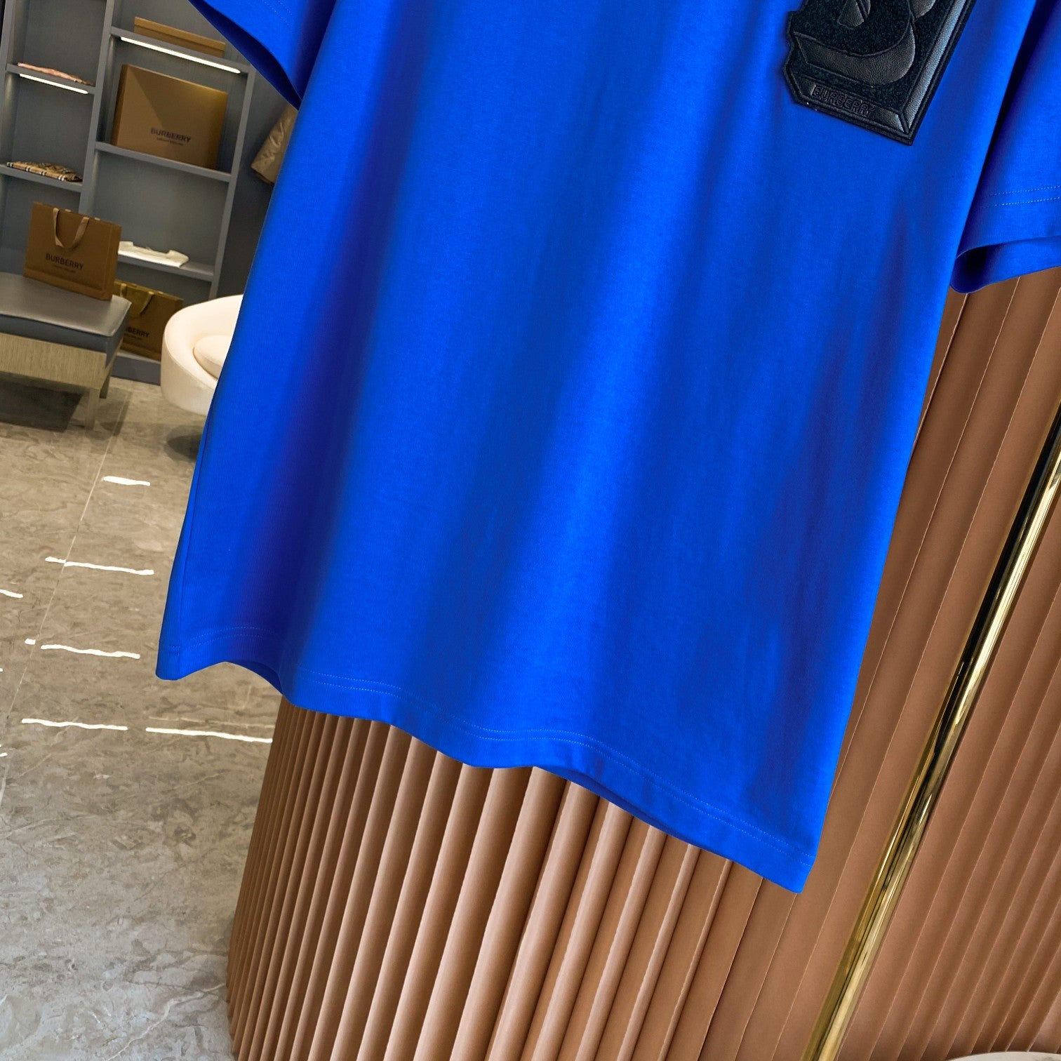 Blue short-sleeve T-shirt side view with chest B logo patch visible.