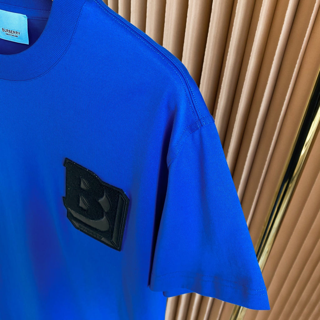 Blue T-shirt with black raised B logo patch on the chest.