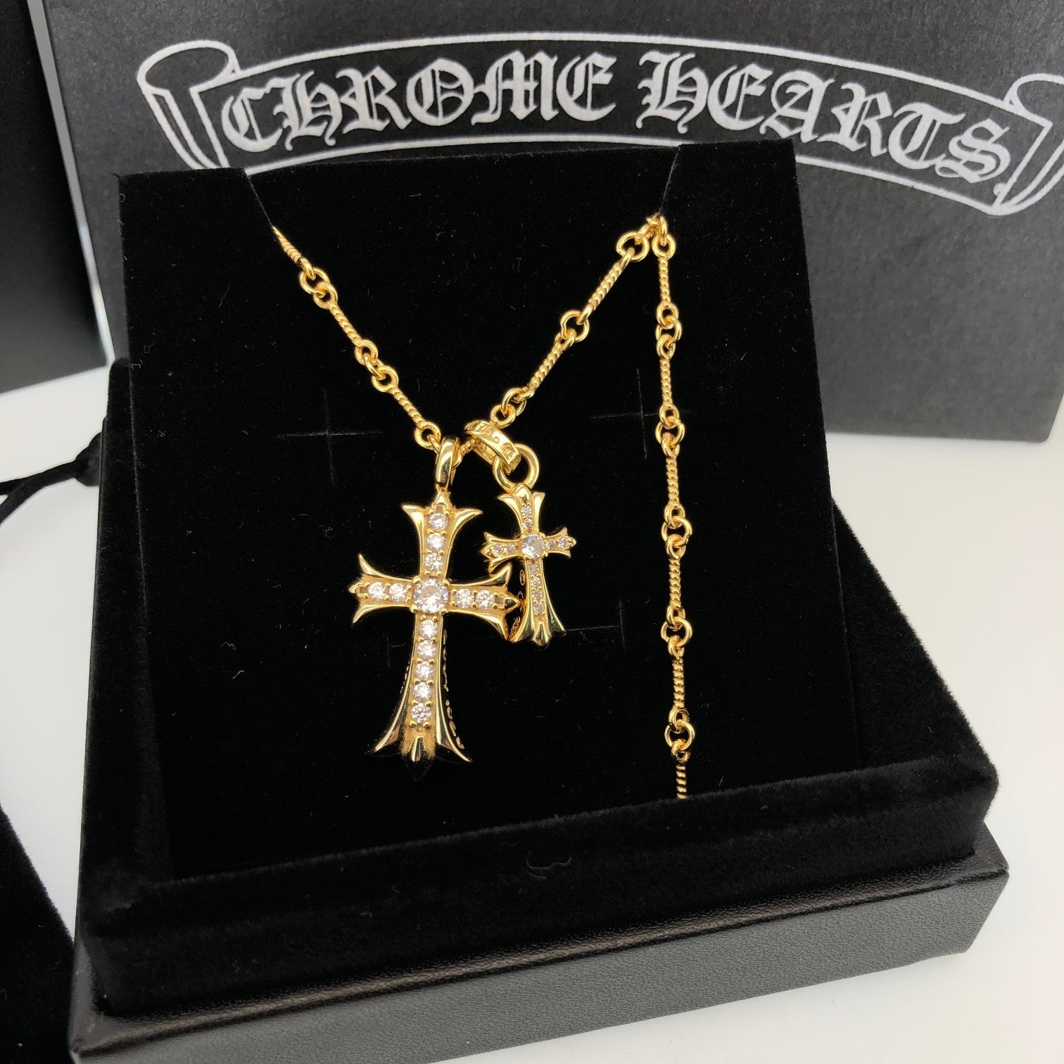 Gold cross pendant necklace with dangling chain on black box
