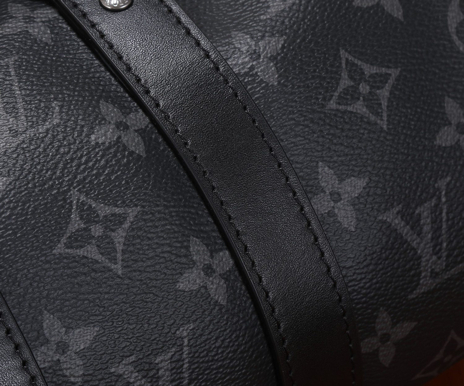 Louis Vuitton monogram bag panel with dark leather trim and visible stitching.