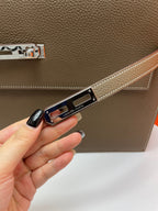 Leather briefcase clasp strap close-up held by hand, metal logo plate