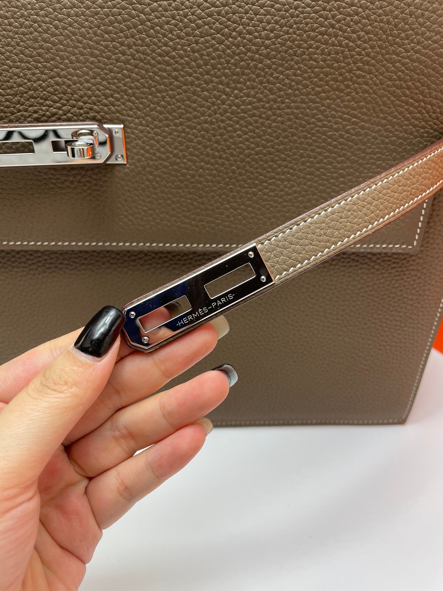 Leather briefcase clasp strap close-up held by hand, metal logo plate