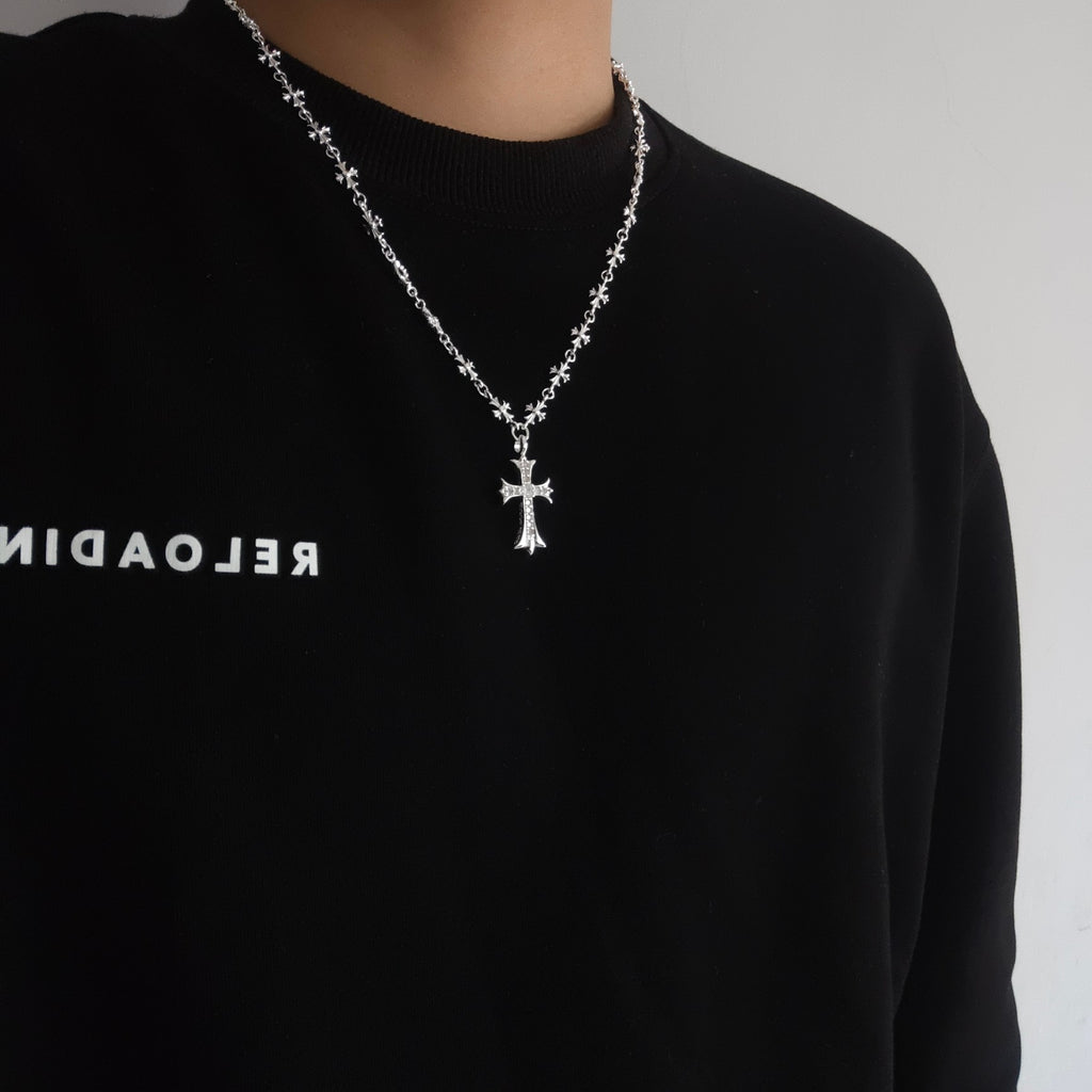 Silver cross pendant necklace worn on a dark crewneck shirt