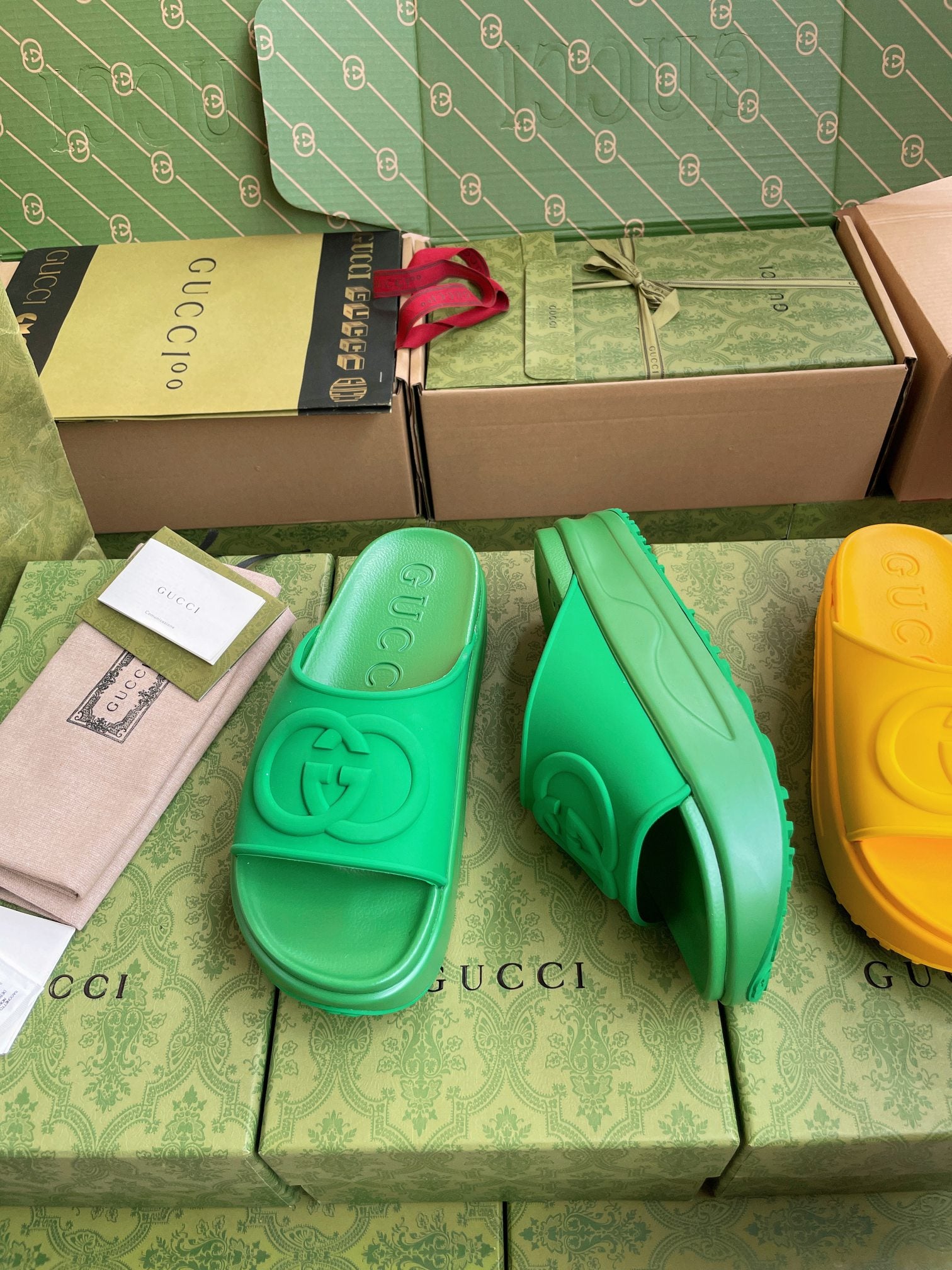 Gucci slide sandals in bright green, with embossed logo footbed; yellow pair visible.