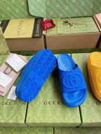 Gucci slide sandals in cobalt blue with embossed logo footbed; yellow side visible.