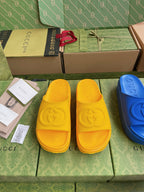 Gucci slide sandals in yellow with embossed logo footbed; blue pair partly visible.