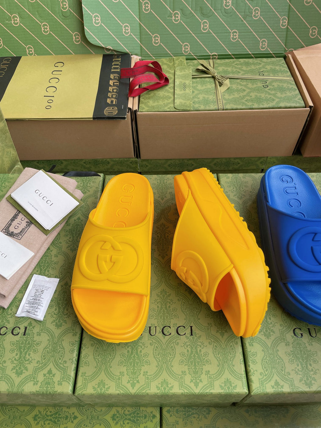 Gucci slide sandals in yellow with embossed logo footbed; blue pair partly visible.