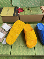Gucci slide sandals in yellow with embossed logo footbed; blue pair partly visible.