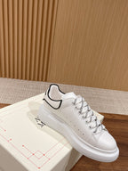 White leather sneakers with black-trim collar, lace-up, and perforated toe