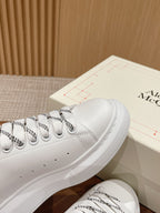 White low-top sneakers with black collar trim and patterned lace details