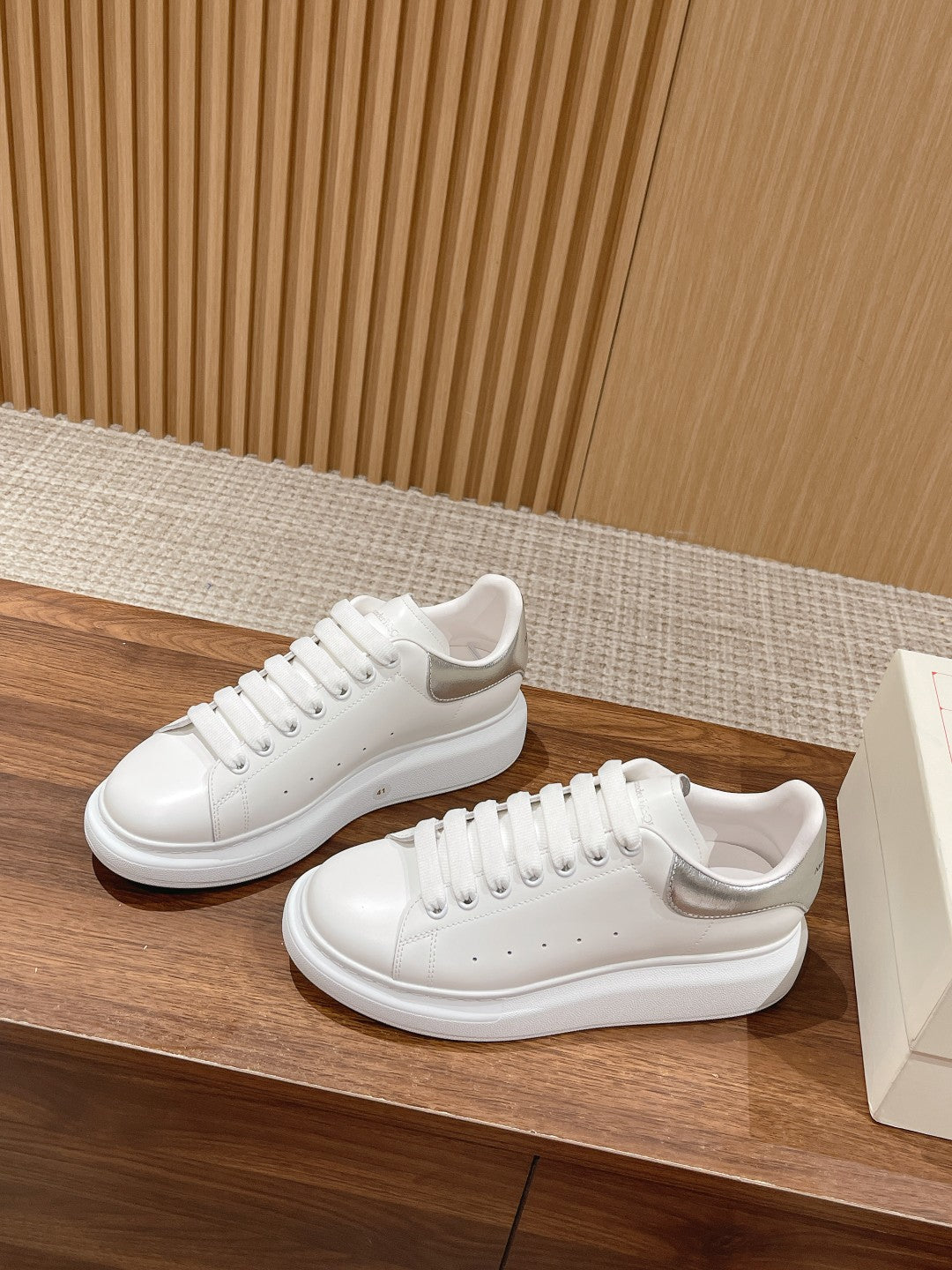 White low-top lace-up sneakers on wooden surface, side view