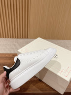 White leather sneakers with black heel detail and lace-up front, low-profile sole