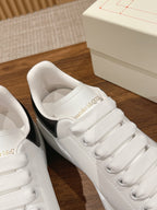 White leather sneaker with cushioned tongue, white laces, and black side panel trim