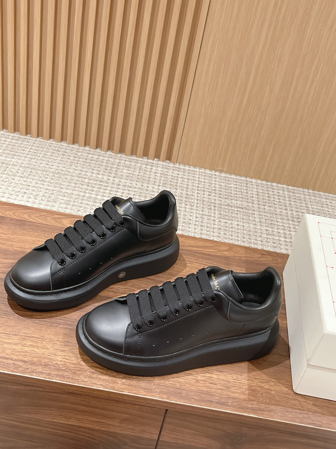 Two black lace-up sneakers on display, featuring thick rubber soles and rounded toes