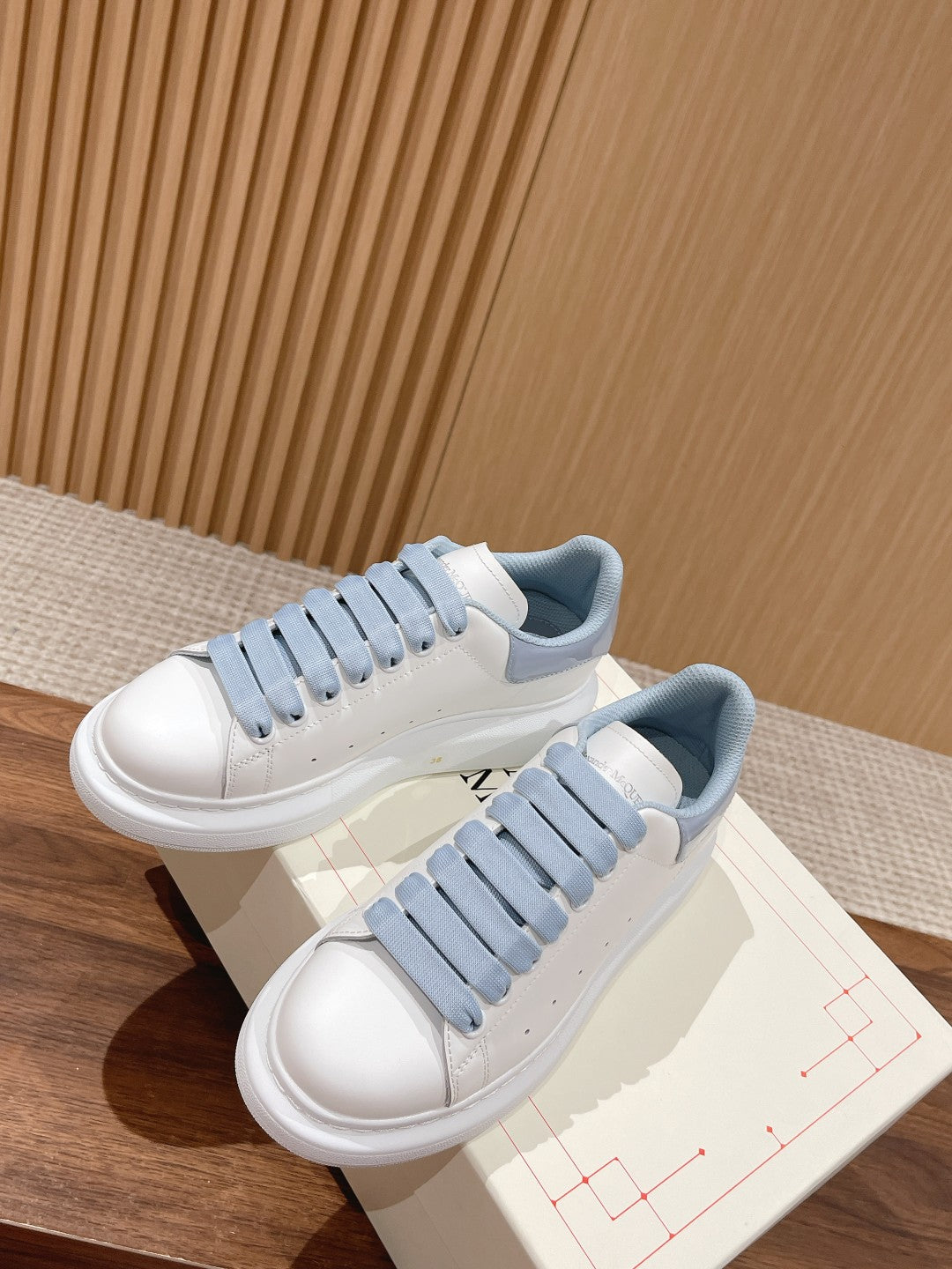 Alexander McQueen low-top sneakers, angled view; white leather with light blue eyelet laces