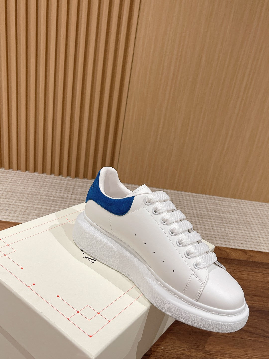 White low-top sneakers with blue suede heel accent and lace-up front