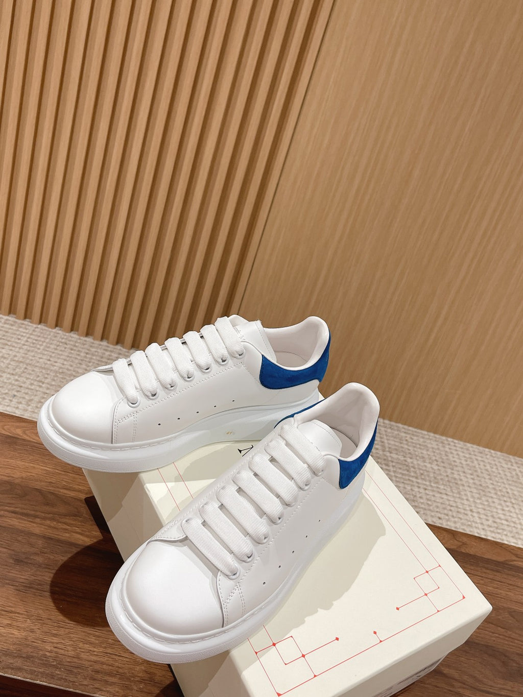 White leather sneakers with blue collar, shown side-by-side on box
