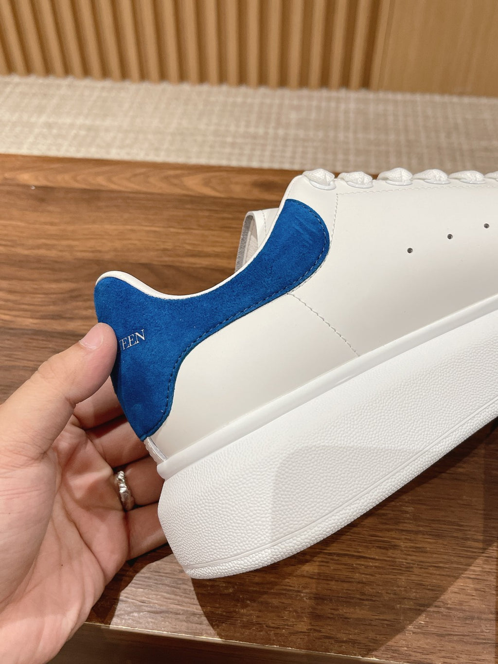White sneaker with blue suede heel panel and white rubber sole, held in hand