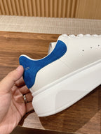 White sneaker with blue suede heel panel and white rubber sole, held in hand